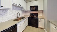 This contemporary apartment offers a blend of comfort and style. The open floor plan maximizes space, with wood-style flooring throughout creating a cohesive look. Large windows in the living areas provide ample natural light, enhancing the sense of spaciousness. The kitchen boasts white cabinetry, black appliances, and a striking herringbone backsplash. The bathroom features a clean, white design with a shower-tub combination. Neutral wall colors and textured ceilings contribute to a fresh, modern aesthetic. The apartment's layout includes multiple rooms, offering versatility for various living arrangements.