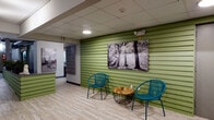 Located at 425 Dayton Towers Drive in Dayton, Ohio, this amenity floor offers residents a well-rounded set of shared facilities designed for comfort and convenience. The welcoming lounge area greets visitors with a vibrant green horizontal-slat accent wall, light wood-style flooring, and colorful teal wicker chairs arranged around a rustic wire-base table. Large black-and-white photographic artwork and a chalkboard wall add personality and creative flair to the social space, making it an inviting spot to relax or connect with neighbors.

The fitness center is generously sized and thoughtfully outfitted with a range of cardio and strength equipment, including treadmills, a stationary bike, and a multi-station weight machine. Motivational wall graphics energize the space, while an exposed industrial ceiling with track lighting, green geometric accent walls, and wall-mounted mirrors contribute to a dynamic workout environment. A mounted flat-screen television and a conveniently placed vending machine add further functionality.

The laundry facility is clean and practical, featuring multiple washers and dryers, a long folding counter, built-in shelving, and light wood-style flooring throughout. Exposed ceiling infrastructure gives the space an honest, utilitarian character while remaining bright and well-organized. Together, these amenities reflect a community-focused environment built to support everyday living.