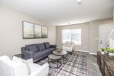 This two-story home offers a thoughtfully designed layout spread across two well-proportioned floors. The main level houses the combined kitchen and dining area, where a galley-style kitchen features white shaker cabinetry, stainless steel appliances including a refrigerator, electric range, and dishwasher, complemented by light wood-look flooring. Adjacent to the kitchen, the dining area benefits from natural light through blinds-covered windows and an overhead chandelier. The living room presents a warm, neutral palette with plush carpeting and a bright window that fills the space with natural light.

Upstairs, the primary bedroom stands out with vaulted ceilings, a ceiling fan, a large window, and soft carpeted floors, creating a comfortable and airy retreat. The second bedroom mirrors the same cozy aesthetic, with carpeting and access to the hallway. Both bathrooms are finished with wood-look flooring and include a full tub-and-shower combination with curved curtain rods. A dedicated closet and hallway provide additional storage and connectivity between rooms. The staircase links both levels efficiently, completing a home that balances practicality with comfortable, neutral-toned design throughout.