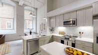 This one-bedroom, one-bathroom residence in Augusta, GA, showcases an industrial-chic aesthetic rooted in its architectural character. Soaring ceilings, polished concrete floors, and whitewashed exposed brick walls define the open-concept living, dining, and kitchen area, flooding the space with natural light through tall, deep-set windows that frame views of the surrounding brick streetscape.

The kitchen is well-appointed with sage-toned shaker cabinetry, white quartz countertops, a subway tile backsplash, stainless steel appliances including a dishwasher, microwave, and range, and a central island ideal for meal prep or casual dining. Pendant lighting adds warmth over both the island and the adjacent dining area, where the soaring ceilings and whitewashed brick create a striking backdrop.

The living area is bright and open, with clean white walls and generous ceiling height that lend a loft-like atmosphere. A built-in mudroom-style nook near the kitchen provides practical storage. The bedroom features the same impressive ceiling height and includes a walk-in closet. The bathroom offers a glass-enclosed shower, a vanity with stone countertop, and polished concrete flooring that ties cohesively to the rest of the home.