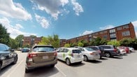 This single-floor space is located at 360 2, set within a well-established brick building complex that rises several stories and features a classic, urban architectural design. The exterior showcases a traditional red brick facade with evenly spaced windows, lending the building a timeless, sturdy aesthetic that blends seamlessly into its surrounding neighborhood.

The property is accompanied by a spacious surface-level parking lot, offering convenient vehicle access for residents and visitors alike. The lot is lined with mature deciduous trees that provide natural shade and greenery, softening the urban environment and contributing to a pleasant outdoor atmosphere. Classic dual-globe lamp posts are positioned throughout the lot, ensuring adequate lighting during evening hours.

The surrounding landscape reflects a well-maintained community setting, with lush tree canopies visible against an open sky. The building's orientation and the open layout of the parking area suggest good accessibility and ease of navigation. Overall, the space presents a functional and established environment within what appears to be a vibrant, mixed-use urban neighborhood, combining practical amenities with architectural character.