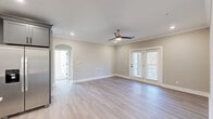 Located at 487 Roanoke Rd in Daleville, Virginia, this well-appointed single-story home offers three bedrooms, two bathrooms, and a thoughtfully designed open floor plan. The heart of the home is a combined kitchen, dining, and living area, where the kitchen stands out with grey shaker-style cabinetry, white quartz countertops, a center island with an undermount sink and stainless steel dishwasher, pendant lighting, and stainless steel appliances including a range and built-in microwave. Light hardwood-style flooring flows throughout the main living spaces, complementing the neutral, warm-toned walls and crown molding. The spacious living room features a ceiling fan, recessed lighting, and elegant French doors that open to a balcony, filling the space with natural light. The primary bedroom is generously sized and includes crown molding, a ceiling fan, and its own French door access. Secondary bedrooms are carpeted, each with ceiling fans and double-door or single closets. Five closets total offer abundant storage, including a dedicated walk-in closet with built-in shelving and rods. The bathrooms are finished with grey vanities, white quartz countertops, and chrome fixtures. Additional spaces include a pantry, laundry area, and connecting hallways that tie the layout together seamlessly.