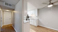 This 1-bedroom, 1-bathroom unit is thoughtfully laid out across a single floor, maximizing every square foot of its compact footprint. The galley-style kitchen is a standout feature, boasting crisp white shaker cabinetry, granite-look countertops, stainless steel appliances including a refrigerator and range, and a skylight that floods the space with natural light. Light wood-look flooring runs throughout the kitchen and living areas, contributing to a clean and cohesive aesthetic. The combined dining and living area offers an open feel, with a ceiling fan and a front entry door that anchors the space. The bedroom is a comfortable size, featuring soft carpet flooring, a window with blinds that frames views of surrounding trees, and direct access to two closets, providing ample storage. The bathroom is well-finished with a white subway tile tub and shower surround, matching granite-look vanity countertop, white shaker cabinetry, and wood-look flooring that ties in with the rest of the unit. Textured ceilings are present throughout, and neutral gray wall tones create a versatile backdrop. A hallway connects the main living spaces to the private bedroom and bathroom, ensuring a functional and organized flow throughout the home.