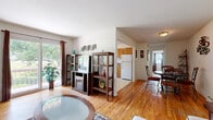 This single-floor, 1-bedroom, 1-bathroom residence offers a thoughtfully arranged layout that maximizes every square foot of its compact footprint. Warm hardwood flooring runs consistently throughout the main living areas, lending a cohesive and inviting feel to the entire space.

The living room serves as the heart of the home, bathed in natural light from a large sliding glass door that opens onto a private balcony overlooking lush greenery. A wall-mounted air conditioning unit ensures year-round comfort, while baseboard heating provides additional warmth.

The living area flows naturally into the dining space, which features an intimate round table set beneath a ceiling light fixture, accented by decorative wall art. Adjacent to the dining room, the kitchen is outfitted with warm oak cabinetry, dark countertops, and white appliances including a range, dishwasher, and full-size refrigerator. A window above the sink brings in natural light, making the kitchen bright and functional.

The spacious primary bedroom offers ample storage with two separate closets, a natural light window, and hardwood flooring that continues from the main living areas.

The bathroom is clean and bright, featuring white tile surround, a bathtub with shower, and a window that introduces natural light into the space.