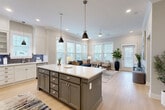 Located in Fort Mill, SC, this thoughtfully designed one-bedroom, one-bathroom residence offers a comfortable and functional single-floor layout. The open-concept kitchen and living area serves as the heart of the home, featuring crisp white shaker cabinetry extending to the ceiling, a slate-blue tile backsplash, stainless steel appliances, and a large center island with seating — ideal for both cooking and casual dining. Pendant lighting and recessed fixtures illuminate the space, while light-toned hardwood flooring flows seamlessly throughout. The living area is lined with multiple windows dressed in white blinds, allowing generous natural light and outdoor views to fill the room. The bedroom is a serene retreat, finished with plush carpet, a ceiling fan, and windows on two walls that bring in additional natural light. The full bathroom is elegantly appointed with a dual-sink vanity, gray cabinetry, white countertops, and a walk-in glass shower featuring floor-to-ceiling marble-style tile. A dedicated closet with built-in shelving and hanging rods provides ample storage, and conveniently includes an in-unit stacked washer and dryer. Crown molding and refined finishes throughout lend the space a polished, cohesive character.