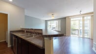 This two-floor residence is thoughtfully designed to balance functional living spaces across its two levels, connected by a carpeted staircase with a white handrail and classic newel post detailing along one side.

The main living area centers around an open-concept layout where the kitchen flows seamlessly into the living and dining spaces. The kitchen is equipped with stainless steel appliances, including a refrigerator, electric range, and over-the-range microwave, all complemented by dark espresso cabinetry and granite-toned countertops. A peninsula with a double basin sink serves as a natural divider between the kitchen and the living area, which features warm hardwood flooring and access to an outdoor balcony through sliding glass doors, allowing generous natural light to fill the space.

The bedrooms are carpeted and well-sized, each featuring windows with outdoor views and baseboard heating. Ceiling light fixtures provide additional illumination. The bathrooms include a vanity with dark cabinetry and a walk-in shower with a glass door. A dedicated laundry area houses a full-sized top-load washer and dryer, adding practical convenience to the layout.