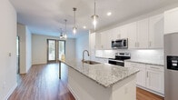 Located at 3250 Buford Hwy in Duluth, GA, this modern single-floor residence offers a well-designed open layout with contemporary finishes throughout. The kitchen is a standout feature, showcasing crisp white shaker cabinetry, a white subway tile backsplash, and a generous granite-topped island with an undermount sink and elegant pendant lighting overhead. A full suite of stainless steel appliances — including a side-by-side refrigerator, electric range, and built-in microwave — completes the space. Hardwood-style flooring flows seamlessly through the main living areas, complementing the bright, neutral color palette. The living area connects to a private balcony through glass-paneled doors, allowing natural light to pour in and providing pleasant outdoor views. Ceiling fans are installed in multiple rooms for year-round comfort. The bedroom features plush carpeting, a ceiling fan, and a well-organized walk-in closet with dedicated shelving and hanging space. The bathroom is appointed with marble-patterned tile surrounding a soaking tub and shower combo, brushed nickel fixtures, and light tile flooring. Clean lines, recessed lighting, and a cohesive modern aesthetic define this thoughtfully finished space.