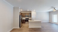 Located on Gold Crest Drive in Greensboro, North Carolina, this single-floor residence offers a thoughtfully designed open-concept layout that seamlessly connects the kitchen and living areas. The kitchen is a standout feature, showcasing rich dark-toned shaker-style cabinetry that extends to the ceiling, light granite countertops, and a classic white subway tile backsplash. A central island with a built-in sink and matching granite surface provides additional workspace and casual seating. The kitchen is fully equipped with a full suite of stainless steel appliances, including a refrigerator, range, and built-in microwave. Warm, wood-look luxury vinyl plank flooring runs throughout the entire space, lending a cohesive and contemporary feel. Crown molding accents the ceilings, adding an elegant architectural touch. The living area is bright and open, highlighted by a ceiling fan with light fixture and glass French doors that provide natural light and direct access to the outdoors. The bathroom features a single vanity with granite countertops, crisp white cabinetry, and a framed mirror above, maintaining the consistent, polished aesthetic found throughout the home. Recessed lighting throughout ensures the space remains bright and welcoming.
