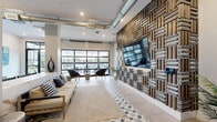 Located at 1775 Ashlar Dr in Fort Collins, Colorado, this single-floor living space showcases a thoughtfully designed interior that seamlessly blends industrial and contemporary aesthetics. The living room serves as the heart of the space, anchored by a striking floor-to-ceiling woven wood and metal accent wall that frames a mounted flat-screen television, creating an immediate visual focal point upon entry.

Exposed silver ductwork runs overhead, lending the space an urban, industrial character that contrasts beautifully with the crisp white walls and polished tile flooring. A standout geometric diamond-patterned tile rug motif grounds the seating area, adding a layer of visual interest underfoot. Natural light pours in abundantly through a full-panel glass garage-style door, which opens directly to an outdoor patio area, seamlessly connecting the interior to the exterior.

The layout includes distinct seating zones, with comfortable sofas and woven accent chairs arranged to encourage conversation and relaxation. A marble-finished bar counter with bar seating adds a refined touch, complemented by dark-framed glass double entry doors that enhance the modern aesthetic. Artwork, tropical plants, and carefully chosen decor elevate the overall ambiance, making this a polished and inviting communal or lounge space.