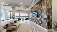 Located at 1775 Ashlar Dr in Fort Collins, Colorado, this single-floor living space showcases a thoughtfully designed interior that seamlessly blends industrial and contemporary aesthetics. The living room serves as the heart of the space, anchored by a striking floor-to-ceiling woven wood and metal accent wall that frames a mounted flat-screen television, creating an immediate visual focal point upon entry.

Exposed silver ductwork runs overhead, lending the space an urban, industrial character that contrasts beautifully with the crisp white walls and polished tile flooring. A standout geometric diamond-patterned tile rug motif grounds the seating area, adding a layer of visual interest underfoot. Natural light pours in abundantly through a full-panel glass garage-style door, which opens directly to an outdoor patio area, seamlessly connecting the interior to the exterior.

The layout includes distinct seating zones, with comfortable sofas and woven accent chairs arranged to encourage conversation and relaxation. A marble-finished bar counter with bar seating adds a refined touch, complemented by dark-framed glass double entry doors that enhance the modern aesthetic. Artwork, tropical plants, and carefully chosen decor elevate the overall ambiance, making this a polished and inviting communal or lounge space.