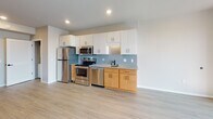 Located at 2225 E Lake St in Minneapolis, MN, this single-floor unit offers a thoughtfully designed layout with clean, contemporary finishes throughout. The kitchen is a standout feature, equipped with stainless steel appliances including a refrigerator, electric range, built-in microwave, and dishwasher. Light wood cabinetry on the lower portion pairs with crisp white upper cabinets, while a soft blue subway tile backsplash and granite countertops add visual interest. Recessed lighting illuminates the space efficiently. A dedicated in-unit laundry closet with a stacked washer and dryer is conveniently integrated just off the kitchen area. The bathroom is well-appointed with a warm wood-toned vanity, white countertop, a full tub-shower combination, and matte black fixtures and hardware that provide a modern accent. Light vinyl plank flooring runs consistently throughout the unit, lending a cohesive and easy-to-maintain aesthetic. The living area is bright and airy, benefiting from large floor-to-ceiling windows that draw in generous natural light and offer open city views. A sliding barn-style door adds a contemporary architectural detail. The overall ambiance is modern, clean, and functional, making efficient use of the single-floor plan.