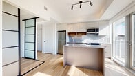Located at 280 Montgomery St in Ottawa's Vanier neighbourhood, this thoughtfully designed one-bedroom, one-bathroom unit offers a modern and efficient layout across a single floor. Light hardwood flooring runs throughout, complementing the bright, white walls and creating a clean, contemporary aesthetic.

The open-concept living area seamlessly integrates the kitchen, dining, and living spaces. The kitchen is equipped with stainless steel appliances, including a full-size refrigerator and microwave, two-tone cabinetry with warm wood accents, a textured tile backsplash, and a central island with a grey countertop that doubles as a breakfast bar. Track lighting overhead adds a modern touch.

Large windows and a glass balcony door flood the living area with natural light and frame expansive views of the Ottawa skyline, offering an elevated urban perspective. The bedroom is defined by a striking frosted glass sliding panel door with a black frame, providing privacy while maintaining the open feel of the space. A mirrored sliding closet adds functionality.

The hallway leads to two closets, in-unit laundry, and a well-appointed bathroom featuring large-format floor tiles, vertical subway wall tiles, black hardware accents, and a glass-enclosed walk-in shower. The overall design balances minimalist style with practical living.