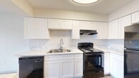 This single-floor residence offers a well-organized layout that efficiently connects the kitchen, living areas, and private rooms. The kitchen is a standout feature, showcasing white shaker-style cabinetry extending to the ceiling for generous storage capacity. Marble-look countertops run throughout, complementing a stainless steel double-basin sink with a pull-down faucet. Black appliances, including an electric range with overhead ventilation, dishwasher, and refrigerator, provide a bold contrast to the bright cabinetry. Wood-look flooring runs through the kitchen and entry areas, adding warmth and durability.

The living area transitions from hard flooring to plush carpeting and features a sliding glass door that invites natural light and outdoor access. A textured ceiling and ceiling-mounted ventilation are present throughout. The bedrooms are carpeted and each include a ceiling fan with light fixture and a window fitted with horizontal blinds, providing both comfort and privacy. The bathroom is appointed with a marble-look vanity countertop, an undermount sink with chrome fixtures, and a tub-shower combination. Overall, the space presents a clean, neutral palette throughout.