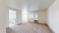 Located at 911 E Beacon Ave in Spokane, WA, this single-floor unit offers three bedrooms and one bathroom within a practical and well-organized layout. The combined living and kitchen area serves as the heart of the home, where a peninsula counter separates the carpeted living space from the tiled kitchen. The kitchen is equipped with light wood cabinetry, white appliances including a range, microwave, refrigerator, and dishwasher, complemented by tile backsplash and a window that invites natural light. The living area features large windows with views of surrounding greenery, wall-unit climate control, and baseboard heating. The spacious primary bedroom includes a mirrored sliding-door closet and connects to the hallway, while additional bedrooms offer generous natural light through multi-pane windows and baseboard heating. The shared bathroom is cleanly appointed with a single-sink vanity featuring light wood cabinetry, a large mirror, tile accents, and a shower-tub combination. Neutral tones, plush carpeting throughout the living and sleeping areas, and consistent lighting give the unit a clean, cohesive ambiance throughout.