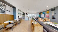 Located at 2801 Grewal Pkwy in Modesto, California, this single-story community clubhouse delivers a sophisticated and welcoming atmosphere through thoughtful design and high-quality finishes. The entrance greets visitors with a soaring double-height lobby framed by floor-to-ceiling glass walls, flooding the space with natural light and offering views of the surrounding exterior. A contemporary chandelier and a statement round table anchor this impressive foyer.

The open-plan interior features light-toned herringbone hardwood flooring throughout, creating visual warmth and continuity. The social lounge area is anchored by a plush sectional sofa, natural wood coffee table, and a pair of cognac leather accent chairs, all set against a paneled gray accent wall adorned with vibrant abstract artwork and large flat-screen televisions. A full-size billiards table completes the entertainment zone.

A generous marble-topped kitchen island with rattan bar stools serves as a central gathering point, illuminated by dramatic woven black pendant lights. The adjacent wet bar features light wood cabinetry, open shelving with curated décor, and a stainless steel undercounter refrigerator. A cozy banquette nook with tufted amber seating and marble-top tables offers an intimate setting for smaller gatherings. Large sliding glass doors open to an outdoor patio, seamlessly blending indoor and outdoor living.
