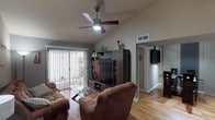 This single-story home offers a well-designed layout with distinct living spaces connected by warm hardwood-style flooring throughout. The living room is a standout area, featuring vaulted ceilings with a ceiling fan and a sliding glass door framed by vertical blinds that provides access to an outdoor patio. A large dark wood entertainment center anchors the room, complemented by a stone-surround electric fireplace with a decorative mantel along the adjacent wall, adding a cozy focal point to the space.

The open sightline from the living room extends into the dining area and toward the kitchen, creating a cohesive flow. The kitchen is equipped with ample white cabinetry, granite-style laminate countertops, a stainless steel sink, and tile flooring, offering practical functionality. A laundry area is conveniently integrated nearby.

The bedroom features hardwood-style flooring, a ceiling fan, vertical blinds over a window, and a wall-mounted television. A second flexible room functions as a home office, complete with crown molding, wall-mounted shelving, a ceiling fan, and a window allowing natural light.

The bathroom includes a tub-shower combination with frosted sliding glass doors. Throughout, ceiling fans, neutral tones, and consistent flooring tie the home together into a cohesive, comfortable living environment.