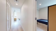 This well-appointed single-floor residence offers two bedrooms and two bathrooms within a thoughtfully designed layout connected by three hallways. The interior is characterized by a clean, modern aesthetic, featuring light wood-tone flooring throughout and crisp white walls that amplify the sense of openness.

The living room serves as the heart of the unit, highlighted by an array of large windows adorned with distinctive circular lattice decorative screens that filter natural light while framing outdoor urban and hillside views. A tray ceiling detail adds architectural depth to the space.

The kitchen is finished with a dual-tone cabinetry scheme combining white upper cabinets and warm wood-grain lower cabinets, complemented by gray quartz countertops and a full suite of stainless steel appliances, including a range, dishwasher, and microwave. A window with matching decorative screening provides natural light.

Both bedrooms are efficiently sized, each featuring built-in platform beds with integrated drawer storage and windows with decorative screens. The two bathrooms mirror each other in design, each equipped with a soaking tub and shower combination, wood-tone vanity cabinetry, and a large mirror, maintaining the unit's consistent modern palette.