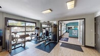 Located at 3050 Kirklevington Dr in Lexington, Kentucky, this single-floor fitness center is a well-equipped amenity space designed to support a comprehensive workout routine. The facility is organized across several interconnected zones, each serving a distinct purpose.

The strength training area features multiple Precor cable machines, a multi-station weight machine, benches, and a rowing machine, all positioned on protective floor mats over light hardwood-style flooring. Windows along the perimeter allow natural light to fill the space, creating an open and energizing atmosphere.

The cardio zone is highlighted by soaring vaulted ceilings with a bold teal accent wall and full-length mirrors that amplify the sense of space. It is equipped with Matrix treadmills, ellipticals, and spin bikes, alongside a wall-mounted television. Motivational phrases are displayed prominently on the walls throughout, reinforcing an active and goal-oriented environment.

A bright sunroom-style lounge area connects to the facility, featuring floor-to-ceiling windows with views of an outdoor courtyard and stone landscaping. A warm wood-paneled ceiling, a bistro table with stools, and a foosball table make this a welcoming space to relax before or after a workout.

The facility also includes a private tanning room equipped with a UV tanning bed, tucked into a dedicated alcove for added privacy. Together, these spaces form a versatile, well-appointed fitness and wellness center.