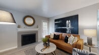 This thoughtfully designed single-floor residence blends contemporary style with everyday comfort across its well-appointed living spaces. Light wood-look flooring flows seamlessly throughout, creating a cohesive and airy feel.

The living room serves as the heart of the home, anchored by a classic fireplace with a white mantel and complemented by large windows with slatted blinds that invite natural light. A striking oversized dark abstract canvas, a warm cognac leather sofa, and a round marble-top coffee table contribute to the room's modern yet inviting ambiance. A decorative starburst mirror adds a bold accent above the mantel.

Adjacent to the living area, an entryway vignette features a richly textured dark wood console with gold-toned hardware, topped by a geometric gold-framed mirror — a refined transitional detail connecting the spaces.

The kitchen is equipped with stainless steel appliances, including a range, microwave, and refrigerator, complemented by gray shaker-style cabinetry and a crisp white subway tile backsplash — a clean, functional design with modern sensibility.

The bedroom offers a serene retreat, highlighted by a plush upholstered bed dressed in layered textiles and accented by a bold gold circular artwork above the headboard, warm bedside lighting, and light-toned flooring.

The bathroom features gray shaker vanity cabinetry, a wide mirror with Hollywood-style lighting, and clean white finishes, delivering a polished and practical space.