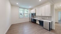 Located at 400 S 40th St in Philadelphia's University City neighborhood, this well-appointed one-bedroom, one-bathroom unit offers a clean, modern aesthetic throughout its single-floor layout. The open-concept kitchen and living area serves as the heart of the unit, featuring stainless steel appliances, a two-tone cabinet design with crisp white uppers and deep navy lowers, a subway tile backsplash, white quartz countertops, and recessed lighting. A large window floods the space with natural light and offers views of surrounding greenery. Wide-plank wood-look flooring runs seamlessly through the main living areas, adding warmth to the bright, neutral palette. The bedroom is a comfortable, well-proportioned room benefiting from multiple windows that invite abundant natural light and outdoor views. A mirrored wardrobe provides practical storage and enhances the sense of space. The bathroom is thoughtfully designed with classic white hexagonal tile flooring, a white vanity with ample counter space, a large mirror, and a window for natural ventilation. A stacked washer unit is conveniently integrated into the bathroom, adding in-unit laundry functionality. Clean white walls and consistent finishes throughout give the unit a cohesive, contemporary feel.
