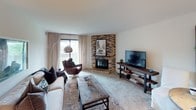 This single-floor residence offers a thoughtfully designed layout across several distinct living areas. The living room serves as the home's focal point, anchored by a striking corner brick fireplace that extends to the ceiling, adding warmth and architectural character to the space. Neutral carpet, large windows with sheer draping curtains, and room for multiple seating arrangements make this an inviting gathering area with ample natural light.

The kitchen is well-equipped with warm wood cabinetry, dark granite countertops, a decorative tile backsplash, and a full suite of stainless steel appliances including a range, microwave, and refrigerator. Track lighting and pendant fixtures illuminate the workspace, while tile flooring adds a practical touch.

The primary bedroom features a bold navy accent wall, carpeted flooring, and windows that bring in natural light. A secondary bedroom offers flexibility as a home office or guest room, complete with built-in wall shelving and a cozy reading nook with a window.

Two full bathrooms each include a tub-shower combination with clean white tile surrounds and vanity storage. The overall aesthetic throughout is cohesive—neutral tones paired with warm wood accents create a comfortable, modern atmosphere.