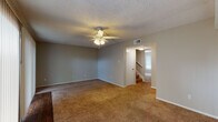 This two-floor residence offers a practical and well-organized layout spread across multiple rooms. The main living area on the ground floor is generously sized, featuring warm beige carpeting, a ceiling fan with integrated lighting, and a textured ceiling. Large sliding glass doors dressed with vertical blinds allow natural light to fill the space. A staircase connects the two floors, with an additional carpeted room nearby offering a ceiling fan and a window with blinds.

The kitchen is efficiently designed with white cabinetry, dark granite-style countertops, a stainless steel sink, a dishwasher, and wood-look flooring. A window above the counter brings in additional natural light, making the space feel open and functional.

The bedrooms are carpeted and equipped with ceiling fans, offering comfortable, quiet spaces. Each room benefits from windows that provide natural light and ventilation.

The bathrooms are clean and straightforward in design. One features a full tub-and-shower combination with white tile surround and chrome fixtures, while another includes a vanity with dark countertops, a framed mirror, and wood-look flooring. A half bath provides additional convenience with matching vanity finishes. Throughout the space, neutral tones and consistent finishes create a cohesive and understated aesthetic.