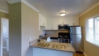 This single-floor residence centers around a thoughtfully designed kitchen that balances functionality and style. The kitchen features granite countertops with warm, neutral toning that extends across both the main workspace and a peninsula counter, providing additional prep space and a casual dining area. White shaker-style cabinetry lines the upper walls, offering generous storage while maintaining a bright, clean aesthetic complemented by crown molding details. Stainless steel appliances include a refrigerator, electric range with oven, and an over-the-range microwave, giving the kitchen a modern, polished look. A stainless steel sink is conveniently positioned along the counter run, with additional lower cabinetry providing further storage. The textured ceiling and flush-mount light fixture provide even illumination throughout the space. The kitchen opens toward adjacent living areas via the peninsula layout, creating an efficient, semi-open flow ideal for everyday use. Neutral wall tones and hardwood-style flooring visible at the kitchen's edge contribute to a cohesive, warm ambiance throughout the home.