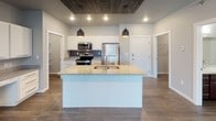 This single-floor residence offers a well-designed layout that balances modern finishes with functional living spaces. The kitchen serves as a central highlight, featuring white shaker-style cabinetry, granite countertops, a gray tile backsplash, and a full suite of stainless steel appliances including a range, over-the-range microwave, and refrigerator. A large kitchen island with an undermount sink and pendant lighting overhead adds both workspace and visual appeal, complemented by a wood-paneled ceiling accent that adds warmth to the area.

The open living area is anchored by a striking stone-clad fireplace with a built-in electric insert, with wood-look flooring running throughout. Natural light enters through windows dressed with vertical blinds. The carpeted bedrooms are comfortable and well-proportioned, each with natural light and baseboard heating. One bedroom includes a ceiling fan, while another features a wall-mounted AC unit.

The bathrooms are finished with dark wood vanities, granite-topped counters, and wood-look flooring. One bathroom includes a walk-in closet with wire shelving, and another features a full tub-shower combination. A dedicated in-unit laundry space houses a full-size washer and dryer with overhead shelving for added storage.