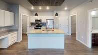 This single-floor residence offers a well-designed layout that balances modern finishes with functional living spaces. The kitchen serves as a central highlight, featuring white shaker-style cabinetry, granite countertops, a gray tile backsplash, and a full suite of stainless steel appliances including a range, over-the-range microwave, and refrigerator. A large kitchen island with an undermount sink and pendant lighting overhead adds both workspace and visual appeal, complemented by a wood-paneled ceiling accent that adds warmth to the area.

The open living area is anchored by a striking stone-clad fireplace with a built-in electric insert, with wood-look flooring running throughout. Natural light enters through windows dressed with vertical blinds. The carpeted bedrooms are comfortable and well-proportioned, each with natural light and baseboard heating. One bedroom includes a ceiling fan, while another features a wall-mounted AC unit.

The bathrooms are finished with dark wood vanities, granite-topped counters, and wood-look flooring. One bathroom includes a walk-in closet with wire shelving, and another features a full tub-shower combination. A dedicated in-unit laundry space houses a full-size washer and dryer with overhead shelving for added storage.