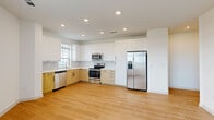 This thoughtfully designed one-bedroom, one-bathroom unit delivers a modern aesthetic through a cohesive combination of light wood flooring, white walls, and recessed lighting. The open-concept kitchen and living area forms the heart of the unit, where the kitchen stands out with two-tone cabinetry—crisp white upper cabinets paired with natural wood lower cabinets—complemented by white countertops and a full suite of stainless steel appliances, including a refrigerator with ice maker, electric range, microwave, and dishwasher. A window above the sink provides natural light.

Near the entry, a built-in nook with a bench seat, lower shoe cubbies, and wall hooks offers a practical and organized arrival space. The bedroom features plush carpet flooring, a ceiling fan, and a wide window with outdoor views, creating a bright and comfortable retreat. An adjacent walk-in closet provides ample storage with built-in shelving and hanging rods.

The bathroom is finished with marble-style tile surrounding the soaking tub and shower, a wood-tone vanity with a white undermount sink, and a large framed mirror, delivering a clean, spa-like atmosphere throughout.