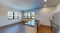 Located at 122 Oakes St SW in the heart of Grand Rapids, Michigan, this thoughtfully designed single-floor unit blends contemporary finishes with functional living. The open-concept kitchen and living area serves as the centerpiece of the space, anchored by a large island with a dark granite countertop, undermount sink, and elegant pendant lighting overhead. The kitchen is fully equipped with stainless steel appliances, including a refrigerator, range, and microwave, complemented by sleek white cabinetry and a tile backsplash. Rich wood-look flooring runs throughout the main living areas, adding warmth to the clean, modern aesthetic. Multiple windows along the living area walls invite abundant natural light and offer views of the surrounding neighborhood. The entryway features a built-in wall-mounted coat rack and a solid wood-finish door with a smart lock. The bedroom is generously proportioned with high ceilings, wood-look flooring, and direct access to both a closet and the bathroom. The bathroom is finished with a granite-topped vanity, a backlit mirror, and chrome fixtures. A separate bonus room with exposed concrete block walls and carpeted flooring provides additional flexible storage or utility space.