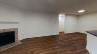 Located at 1924 Teal Trce in Pittsburgh, Pennsylvania, this single-floor unit offers 590 square feet of thoughtfully arranged living space across one bedroom and one bathroom. The combined kitchen and living area serves as the heart of the home, where rich hardwood-style flooring flows throughout. The living room is anchored by a tile-surround fireplace and a sliding glass door that floods the space with natural light and provides views of a lush green hillside. The kitchen is equipped with stainless steel appliances—including a refrigerator, electric range, and over-the-range microwave—complemented by white cabinetry, dark countertops, a peninsula with an integrated sink, and white tile flooring. The entryway features the same hardwood-style flooring and recessed lighting for a clean, welcoming entry. The primary bedroom measures 170 square feet and is finished with neutral carpet and a sliding glass door offering additional outdoor access and natural light. The bathroom is appointed with a floating vanity featuring white shaker-style cabinetry, dark hardware, a gold-toned faucet, white countertop, and tile flooring. Crown molding and white baseboards are present throughout, lending a polished, consistent finish to the entire unit.