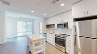 Located at 1230 N Henry St in Alexandria, VA, this two-bedroom, two-bathroom residence offers a thoughtfully designed single-level layout. The open-concept kitchen and living area serves as the heart of the home, featuring crisp white cabinetry with warm wood accent shelving, a white tile backsplash, stainless steel appliances including a refrigerator, range, microwave, and dishwasher, and light-toned hardwood-style flooring that flows throughout. Recessed lighting illuminates the space with a clean, modern feel.

Both bedrooms are bright and welcoming, with large windows fitted with blinds that invite natural light while providing privacy. The primary bedroom offers a generous footprint with direct access to a well-appointed en-suite bathroom featuring a glass-enclosed shower, white vanity, and a walk-in closet. The second bathroom echoes the same clean aesthetic with a white vanity, open shelving, and hardwood-style flooring.

A private balcony extends the living space outdoors, offering views of the surrounding streetscape and landscaped courtyard within the community. Four closets throughout the residence provide ample storage. The overall ambiance is modern and light-filled, with a neutral palette and contemporary finishes that create a versatile, move-in-ready environment.