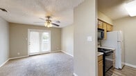 This single-floor, 2-bedroom, 1-bathroom residence offers a practical and comfortable layout designed to maximize every square foot. The living area greets you at the entrance, featuring plush wall-to-wall carpeting, neutral warm-toned walls, a textured ceiling, and a ceiling fan with integrated lighting. French doors flood the space with natural light and provide direct outdoor access, complementing the open, airy feel of the room. The kitchen is thoughtfully appointed with light wood cabinetry, a tile backsplash, black appliances including a range and dishwasher, a white refrigerator, and a tall pantry cabinet for added storage. Wood-look flooring ties the kitchen together neatly. The spacious primary bedroom continues the carpeted theme and benefits from its own ceiling fan, while a dedicated walk-in closet offers generous storage. The second bedroom also features carpeting, a ceiling fan, a natural light window, and closet access. The full bathroom includes a white tiled tub-shower combination, wood-look flooring, and clean, bright finishes throughout. A utility room and additional closet round out the functional amenities of this well-laid-out residence, ensuring ample storage and everyday practicality.