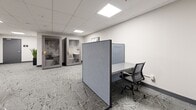 Located at 1475 Whites Rd in Pickering, Ontario, this professional office suite offers a thoughtfully designed single-floor workspace ideal for productive and focused work. The space is finished with a striking patterned carpet in grey tones, crisp white walls, and a suspended tile ceiling fitted with recessed LED panel lighting that ensures bright, even illumination throughout.

A standout feature is the large-scale world map mural adorning one wall, adding a bold and globally inspired visual element to the space. Two enclosed privacy pods provide self-contained areas for focused individual work or private calls, each equipped with a built-in work surface and interior lighting. A fabric-panelled partition divider creates a semi-private workstation area furnished with a desk and ergonomic mesh chair, offering a flexible open-plan working option.

The suite also includes a casual seating area with round tables and chairs, suitable for informal meetings or collaborative sessions. Curated abstract artwork is displayed on the walls, contributing to a polished and professional atmosphere. A potted plant near the entrance adds a touch of greenery. The space is accessed through a grey-panelled door and is well-suited for coworking, small team operations, or private office use.