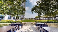 Located at 360 State St in the heart of New Haven, CT, this beautifully landscaped outdoor amenity terrace offers a serene urban retreat set against the backdrop of a striking modern high-rise. The terrace is thoughtfully designed to blend lush greenery with functional outdoor living spaces, creating a resort-like atmosphere above the city streetscape.

A generously sized, meticulously maintained lawn serves as the central feature, bordered by wide stone-paved walkways that invite leisurely strolls throughout the space. Vibrant flower beds burst with seasonal color, interspersed with neatly trimmed hedgerows and mature trees that provide natural shade and a sense of privacy.

Dedicated outdoor dining areas are furnished with tables and chairs, ideal for al fresco gatherings. A pergola structure anchors one section of the terrace, offering a shaded retreat framed by additional plantings and raised garden beds. A pool area with surrounding lounge seating provides another focal point for recreation and relaxation.

The terrace benefits from open sky exposure, filling the space with abundant natural light throughout the day. Panoramic views of the New Haven skyline and surrounding cityscape are visible from multiple vantage points, enhancing the elevated ambiance. The overall design seamlessly integrates architectural structure with natural elements, offering residents a refined and versatile outdoor environment.
