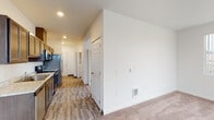 This single-floor residence offers a practical and cohesive layout connecting the main living areas through a central hallway. The living area is generously proportioned, finished with plush wall-to-wall carpeting and crisp white walls that create a bright, clean atmosphere. A vertical-blind window allows natural light to filter in, while a private exterior door provides direct outdoor access with views of the surrounding neighborhood, adding an element of openness to the space.

The kitchen is efficiently designed with dark espresso-toned cabinetry offering ample upper and lower storage. Light stone-patterned countertops complement the full suite of stainless steel appliances, including a refrigerator, electric range, over-the-range microwave, and dishwasher. Wood-look plank flooring runs through the kitchen and hallway, providing a durable and visually cohesive transition between areas.

The bathroom is well-equipped, featuring a single-sink vanity with a marble-style countertop and dark cabinetry, a wide mirror, wood-look tile flooring, and a combined tub and shower enclosure. A frosted window provides natural light while maintaining privacy. Recessed lighting throughout the unit ensures consistent, functional illumination across all areas.