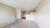 This single-floor, one-bedroom, one-bathroom unit offers a practical and efficiently organized layout. The living room features neutral-toned carpet, textured ceilings, large windows with horizontal blinds that allow natural light to filter in, and a wall-mounted HVAC unit. The space opens toward the kitchen area, which is separated by a half-wall breakfast bar with a light-toned countertop. The kitchen is equipped with blue-gray cabinetry, a white electric coil range, a full-size refrigerator, a single-basin sink, and a range hood overhead. Hardwood-style flooring runs through the kitchen and connects to the dining area, which features a ceiling fan with light fixture. The bedroom is a comfortable size, carpeted, and includes a window that brings in natural light. A dedicated closet provides storage with dual hanging rods across two sections and hardwood-style flooring. The full bathroom includes a single-sink vanity with gray cabinetry, a toilet, and a full tub-shower combination with a white surround, complemented by hardwood-style flooring throughout.