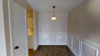 This single-floor, 1-bedroom, 1-bathroom residence offers a well-utilized layout designed to maximize comfort and functionality. The main living area features plush carpeting underfoot and a textured ceiling overhead, lending a warm, cozy feel to the space. A standout design element is the classic wainscoting that lines the lower portion of the walls, adding a touch of traditional character and visual interest. A pendant light fixture hangs from the ceiling, providing focused ambient lighting that complements the room's charm.

Neutral wall tones throughout create a clean, versatile backdrop suitable for a variety of décor styles. An open doorway visible from the main area leads into an adjacent space equipped with cabinetry and what appears to be a countertop, suggesting a functional kitchen or utility area with ample storage. The layout flows naturally between spaces, maintaining a sense of openness despite the compact footprint.

Overall, this residence balances practicality with classic design touches, making it an efficient and inviting living space well-suited for individuals or couples seeking a comfortable single-floor home.
