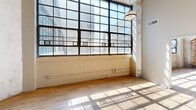 Located at 2320 E Superior Ave in Cleveland, Ohio, this industrial loft-style unit blends historic character with modern updates across a well-proportioned single-floor layout. The space is defined by its soaring ceilings with exposed ductwork and piping, warm hardwood-style flooring, and dramatic floor-to-ceiling factory windows that flood the interior with natural light and offer urban views of the surrounding cityscape.

The open living area showcases original exposed brick walls alongside raw concrete columns, lending an authentic industrial aesthetic. The kitchen features rich dark-stained wood cabinetry with ample storage, granite-look countertops, and a full suite of stainless steel appliances, including a refrigerator, range, microwave, and dishwasher, all set against a bold yellow accent wall beneath elevated ceilings with industrial pendant lighting.

The generously sized primary bedroom provides ample space for furnishings, while the second bedroom offers a functional layout with pendant lighting and direct access to additional rooms. Both bathrooms are finished with tile flooring, vanities with storage, and walk-in shower stalls. A dedicated closet adds practical storage to complete this distinctive urban living space.