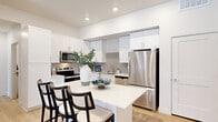 This thoughtfully designed two-bedroom, one-bathroom residence offers a comfortable and modern living experience across a single floor. The layout flows seamlessly from room to room, connecting key living spaces with functionality and style.

The kitchen is a standout feature, showcasing crisp white shaker cabinetry extending to the ceiling, sleek quartz countertops, and a full suite of stainless steel appliances including a range, over-the-range microwave, and refrigerator. A gray tile backsplash adds texture and visual contrast, while a central island with bar seating provides an ideal space for casual dining and meal prep. Light wood-tone flooring ties the space together.

The living room is bright and welcoming, benefiting from natural light that pours through a glass door opening to a private outdoor balcony area — a functional extension of the interior living space.

Both bedrooms are well-proportioned and serene, each featuring large windows that invite natural light. The primary bedroom is generously sized and is accompanied by a dedicated walk-in closet with built-in shelving and hanging rods for organized storage.

The full bathroom is clean and functional, featuring a white vanity with storage, a tub-shower combination, and warm wood-look flooring that echoes the rest of the home. Recessed lighting throughout the residence adds to the bright, contemporary ambiance.