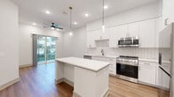 Located at 1201 Hillside Avenue in Nashville, TN, this modern 1-bedroom, 1-bathroom unit offers a thoughtfully designed open-concept layout finished with warm wood-look flooring throughout. The combined living, dining, and kitchen area serves as the heart of the space, highlighted by a central white quartz island with pendant lighting overhead and a ceiling fan that enhances airflow and comfort. The kitchen is outfitted with crisp white shaker cabinetry reaching toward the ceiling, a classic subway tile backsplash, and a full suite of stainless steel appliances including a gas range, microwave, dishwasher, and refrigerator. Sliding glass doors connect the living area to an outdoor balcony, inviting natural light deep into the space. The bedroom is a comfortable, well-proportioned room with a window providing additional natural light. A walk-in closet with wire shelving systems offers generous storage. A second closet adds further organization options. The bathroom features a white vanity with quartz countertop, a black-framed mirror, matte black fixtures, and a tiled shower. A dedicated laundry area and utility room complete the practical layout of this well-appointed Nashville residence.