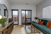This single-floor residence offers a thoughtfully designed layout that balances open communal spaces with private retreats. The kitchen serves as a functional centerpiece, featuring two-tone cabinetry — white uppers paired with warm wood-grain lowers — complemented by a white subway tile backsplash, light quartz countertops, stainless steel appliances, and a peninsula island that provides additional workspace and casual seating. Light wood-style flooring flows throughout, adding warmth to the modern aesthetic.

The living area is bright and inviting, benefiting from floor-to-ceiling windows that frame urban cityscape views and allow ample natural light to fill the space. A sliding barn-style door connects to adjoining areas, adding a stylish architectural detail.

Two well-proportioned bedrooms each feature plush carpeting, large windows with city views, and ceiling fans. The primary bedroom includes space for a sitting area, while both rooms offer a calm, neutral palette suited to restful living.

The bathroom presents a clean, contemporary design with wood-look tile flooring, large-format gray wall tiles, and a frameless glass-enclosed walk-in shower. Throughout the residence, the overall ambiance is polished, modern, and urban.