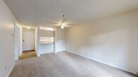 Located at 1111 47th St SE in Everett, Washington, this one-bedroom, one-bathroom unit offers a practical and well-organized single-floor layout. The living room is a comfortable, open space featuring plush carpeting, a ceiling fan with light fixture, and a textured ceiling. A sliding glass door fills the room with natural light and provides access to an outdoor patio area with views of surrounding greenery. The semi-open kitchen is defined by a breakfast bar countertop, overhead cabinetry, and under-cabinet lighting, connecting seamlessly to the living area. The bedroom is a well-proportioned room with carpet flooring, a baseboard heater for efficient heating, a window that brings in natural light and outdoor views, and a built-in closet with sliding doors offering ample storage. The bathroom features wood-look vinyl plank flooring, a white vanity with stone-toned countertop, a large wall mirror with overhead lighting, and clean white finishes throughout. A hallway connects the main living spaces and provides additional flow to the layout. Overall, the unit presents a clean, neutral palette with functional features suited for comfortable everyday living.