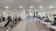 Located in Spring, TX, this single-floor fitness center is designed to support a wide range of workout routines in a clean, modern environment. The space features durable rubber-speckled flooring throughout, providing both safety and functionality for high-intensity exercise. Recessed lighting brightens the entire area, while multiple windows along the walls allow natural light to filter in, offering views of the surrounding outdoor greenery.

The cardio zone is well-stocked with multiple Spirit-brand treadmills, elliptical trainers, and stationary recumbent bikes, offering members a variety of low- and high-impact options. A dedicated strength training section houses a multi-station cable machine system, a rowing machine, a weight bench, and additional resistance-based equipment. A freestanding heavy punching bag adds a functional fitness and combat training element to the space.

Climate control is provided by a wall-mounted mini-split unit, ensuring comfort year-round. French doors at one end of the facility provide access and additional natural light. A wall-mounted television and motivational wall art contribute to the welcoming atmosphere. The open layout allows for easy movement between equipment zones, making this fitness center a comprehensive and accessible facility for users of all fitness levels.