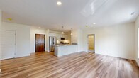 Located at 1471 Route 9 in Halfmoon, NY, this single-floor residence offers a thoughtfully designed open-concept layout across a generous footprint. The combined kitchen and living area serves as the heart of the home, featuring light-toned hardwood-style flooring that flows seamlessly throughout. The kitchen is equipped with stainless steel appliances, including a refrigerator, microwave, and range, complemented by crisp white cabinetry, granite countertops, a central island with a sink, and pendant lighting overhead. A solid wood entry door adds a warm, distinctive touch to the entryway. The living area is bathed in natural light through a pair of large windows overlooking lush greenery. Both bedrooms are carpeted for comfort, with the primary bedroom offering generous proportions and access to a dedicated closet. The two bathrooms are finished with granite-topped vanities, gray cabinetry, and hardwood-style flooring, with one bathroom featuring accessibility-friendly grab bars. An additional closet provides practical storage. The overall aesthetic is clean and modern, with a neutral color palette of whites and soft creams creating a bright, welcoming atmosphere throughout.
