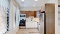 This contemporary single-floor unit offers a thoughtfully designed layout across three rooms, combining modern finishes with a clean, minimalist aesthetic. Light wood-tone laminate flooring runs throughout the entire space, lending a warm and cohesive feel to every room.

The kitchen is a standout feature, showcasing a two-tone cabinet design with rich walnut-finish upper cabinets and crisp white lower cabinetry. A white quartz countertop, subway tile backsplash, and a matte black spring-neck faucet with an undermount sink add refined detail. Stainless steel appliances — including a refrigerator, electric range, built-in microwave, and dishwasher — complete the fully equipped space. Natural light filters in through a large adjacent window with horizontal blinds.

The open living area is bright and airy, featuring recessed lighting and a bank of three large windows that fill the room with natural light and offer views of the surrounding area. A wood-tone door adds a touch of warmth against the white walls.

The sleeping quarters include a bedroom equipped with a modern gold-accented ceiling fan, recessed lighting, and a closet with a rod and shelf system. An additional room offers clean white walls, recessed lighting, and ample flexibility for various uses. The unit presents a cohesive modern design throughout.
