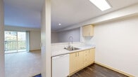 Located in Seattle's Greenwood neighborhood, this one-bedroom, one-bathroom unit offers a well-organized single-floor layout designed to maximize functionality. The kitchen and living area share an open, combined space anchored by light maple cabinetry, a marble-style countertop, a stainless steel sink with a modern pull-down faucet, and white appliances including a dishwasher, range, and refrigerator. A skylight overhead fills the kitchen with natural light, while dark hardwood-style flooring grounds the space with a clean contrast. The living area flows naturally from the kitchen and features carpet flooring and a sliding glass door that invites natural light and outdoor access. The bedroom is a calm, carpeted retreat with a window allowing ample natural light and a closet that houses a stacked in-unit washer and dryer—a practical convenience. The bathroom is finished with a full soaking tub and shower combo, a curved chrome curtain rod, and dark wood-style flooring consistent with the rest of the unit. A hallway connects all areas smoothly, completing a thoughtfully arranged floor plan suited for comfortable everyday living.