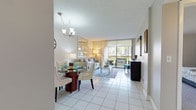 Located at Aventura Harbor, this single-floor residence offers a well-organized layout that balances comfort and functionality throughout its thoughtfully designed spaces. Large-format white tile flooring runs through the main living areas, reflecting natural light and creating a clean, cohesive aesthetic.

The open-concept living and dining area is anchored by floor-to-ceiling sliding glass doors that lead to a private balcony, offering views of lush greenery and palm trees. A chandelier illuminates the dining space, while the living room benefits from abundant natural light streaming in through the expansive glass facade. The balcony provides additional outdoor seating, extending the living space.

The kitchen features white cabinetry, granite countertops, and a full suite of white appliances including a dishwasher, range, microwave, and refrigerator. Tile flooring continues throughout, maintaining a bright, functional workspace.

The spacious bedroom is finished with plush carpeting and includes direct balcony access, adding to its airy feel. A walk-through closet leads to the bathroom, which is equipped with a glass-enclosed tub and shower combination, granite vanity, and white cabinetry.

A stacked washer and dryer unit is conveniently housed within the residence, completing this well-appointed home.