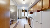 Located at 301 W 1st St in downtown Duluth, Minnesota, this one-bedroom, one-bathroom unit offers an efficient and well-organized layout across a single floor. The open-concept living area seamlessly integrates the kitchen, dining, and living spaces into one cohesive room, maximizing functionality. The kitchen is equipped with warm-toned wooden cabinetry extending to the upper walls, a white electric range, dishwasher, refrigerator, double sink with light countertops, and a built-in microwave. A notable feature is the in-unit washer and dryer, conveniently positioned within the kitchen corridor. Pendant globe light fixtures illuminate the main living area, which receives natural light through a large window framed in rich wood trim. The bedroom is a cozy, private space featuring a double closet with paneled doors and a distinctive interior window with warm wood framing that connects to the entry area. The bathroom is finished with terrazzo-style tile flooring, a wood-trimmed vanity with a granite-top sink, and an open walk-in shower. Light gray walls throughout the unit create a neutral, calm ambiance, complemented by light-toned flooring that unifies the space.